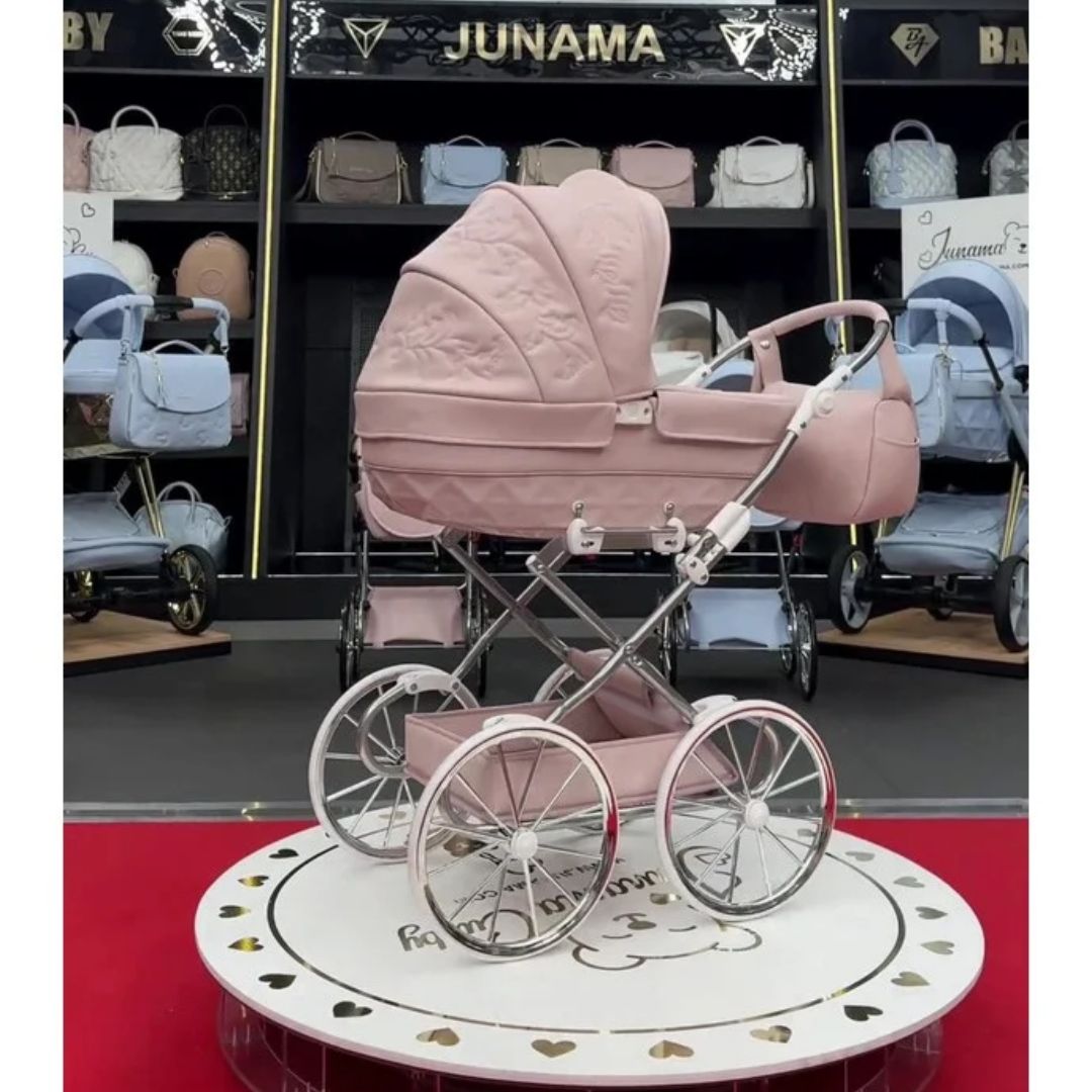 Carrito de muñeca Enzo Mini rosa con capota bordada, chasis cromado y ruedas grandes de estilo clásico.